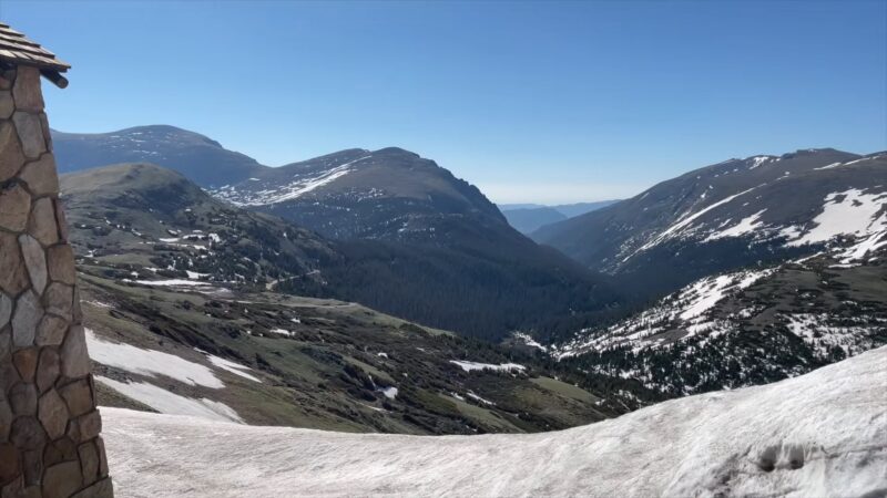 Snow-covered mountains and lush green valleys in Rocky Mountain National Park, Colorado, viewed from a stone shelter